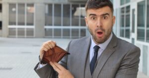 Man in a suit looking surprised while showing an empty wallet, symbolizing challenges of starting a business in Canada with no money.