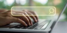 Hands typing on a laptop keyboard with a glowing yellow search bar graphic overlayed.