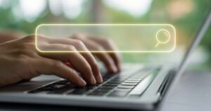 Hands typing on a laptop keyboard with a glowing yellow search bar graphic overlayed.