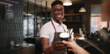 Smiling barista handing a takeaway coffee to a customer in a café