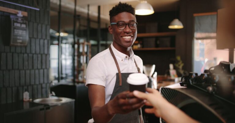 Smiling barista handing a takeaway coffee to a customer in a café