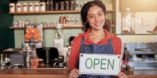 Business owner holding an open sign inside a café.