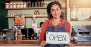 Business owner holding an open sign inside a café.