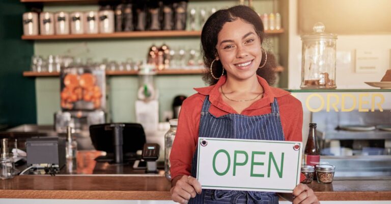 Business owner holding an open sign inside a café.