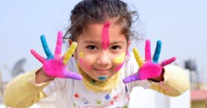 Child showing colorful paint-covered hands.