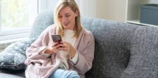 Woman smiling while looking at her phone on a couch.