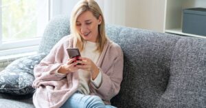 Woman smiling while looking at her phone on a couch.