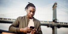 How to market your business on Facebook Man using a smartphone outdoors with a bridge in the background.