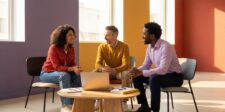 Three professionals discussing landing page strategy around a laptop in a bright, modern meeting space.