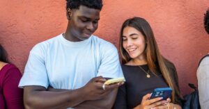 Two people looking at smartphones together while discussing digital content.