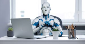 Humanoid robot sitting at an office desk with a laptop, representing AI, automation, and the future of work.