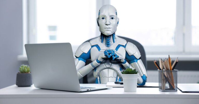 Humanoid robot sitting at an office desk with a laptop, representing AI, automation, and the future of work.