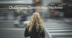 Graphic showing a woman standing at a crosswalk with blurred traffic in the background and the headline, “Challenging Times to be a Marketer.”