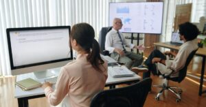 Three coworkers reviewing website or marketing information on computer screens during an office discussion.