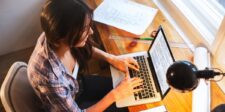 How to make money blogging legitimately Woman working on a laptop at a wooden desk with papers, rulers, and a desk lamp nearby.