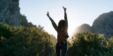 Three people sitting on a bench viewing a large wall display filled with photos of diverse faces. Today 4:36 PM Woman with a backpack raising both arms in a victory pose while standing between mountains at sunrise.