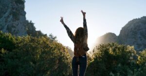 Three people sitting on a bench viewing a large wall display filled with photos of diverse faces. Today 4:36 PM Woman with a backpack raising both arms in a victory pose while standing between mountains at sunrise.