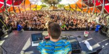 DJ performing on an outdoor festival stage in front of a large crowd.