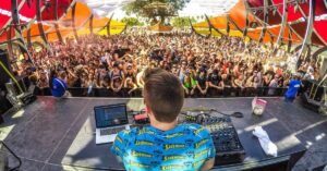 DJ performing on an outdoor festival stage in front of a large crowd.