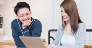 Two smiling adults looking at a laptop together at a table, representing online browsing, internet use, or digital research.