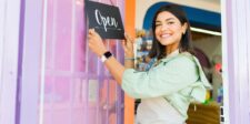 Smiling small business owner hanging an open sign at a storefront, representing a quick SEO guide for local businesses