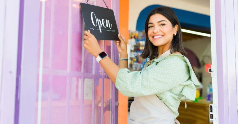 Smiling small business owner hanging an open sign at a storefront, representing a quick SEO guide for local businesses