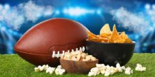 Football, chips, pistachios, and popcorn on turf in a stadium setting, representing Super Bowl viewership trends and game-day audiences.