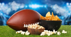 Football, chips, pistachios, and popcorn on turf in a stadium setting, representing Super Bowl viewership trends and game-day audiences.