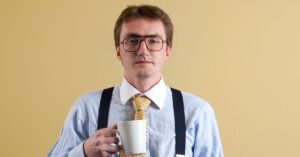 Business professional wearing glasses and holding a coffee mug against a plain background.