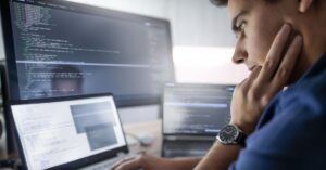 Website administrator reviewing code and multiple computer screens, illustrating website security monitoring and maintenance.