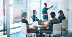 Marketing team discussing strategy around a conference table while a presenter points to a planning board.