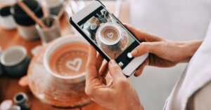 Person photographing a cup of coffee with a smartphone for a social media post.