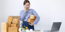 Small business owner packing shipping boxes while talking on the phone beside a laptop.