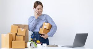 Small business owner packing shipping boxes while talking on the phone beside a laptop.