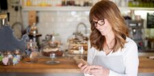 Small business owner smiling while using a smartphone in a café, representing local business marketing and online visibility