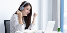 Best AI writing assistant: six tools compared by output quality Woman wearing headphones smiling while using a laptop at a bright desk near a window.