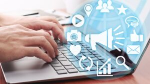 Hands typing on a laptop with many social icons, illustrating the job of a social marketer