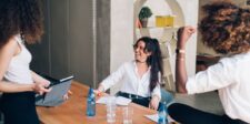 A group of young professionals engaged in a lively discussion, smiling and sharing ideas around a table, embodying the concept of "gamify your life" by turning daily tasks into enjoyable and rewarding experiences.