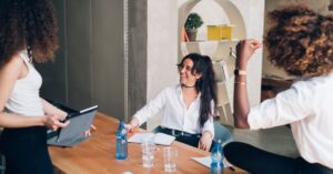 A group of young professionals engaged in a lively discussion, smiling and sharing ideas around a table, embodying the concept of "gamify your life" by turning daily tasks into enjoyable and rewarding experiences.