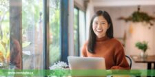 Smiling woman using a laptop in a cozy, plant-filled café, representing productivity and comfort, as discussed in our MacBook Air M3 review.