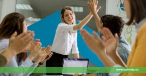 A woman in a white shirt smiles while giving a high-five to a colleague during a meeting, symbolizing teamwork and successful collaboration. Other team members are clapping, showing support and recognition for the achievement. A laptop is visible on the table, indicating a productive work environment. The image reflects themes of entrepreneurship and leadership, highlighting the importance of fostering a supportive and motivated team.