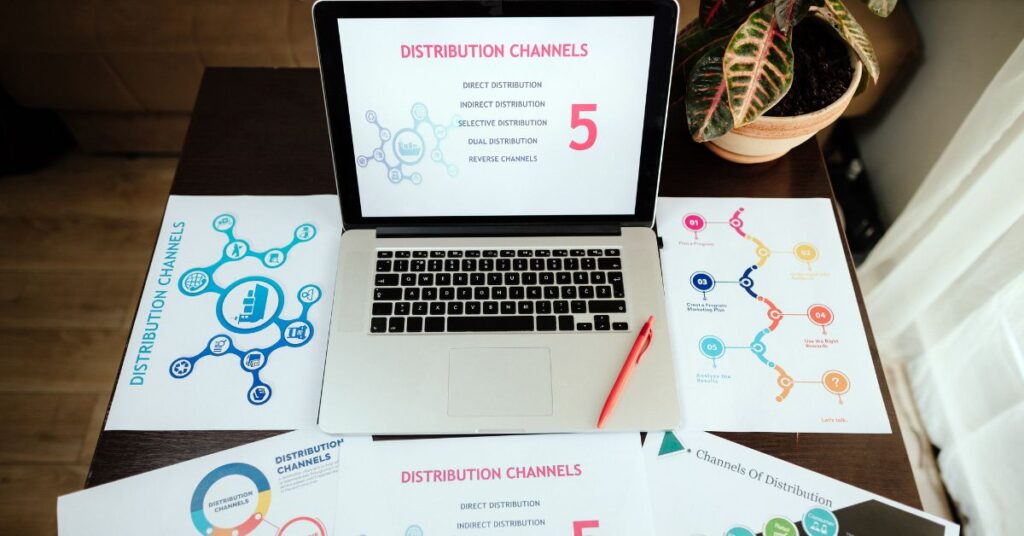 Guide to Distribution Channels and How to Use Them" features a laptop displaying a slide with the title "Distribution Channels" and five types of distribution channels: Direct Distribution, Indirect Distribution, Selective Distribution, Dual Distribution, and Reverse Channels. The laptop is surrounded by various printed diagrams and charts related to distribution channels, including one labeled "Plan & Progress," emphasizing the strategic planning and analysis involved in utilizing distribution channels effectively. A red pen rests on one of the papers, and a potted plant is partially visible in the background. The overall setup suggests a workspace focused on understanding and optimizing distribution channels.