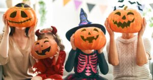 Family dressed in Halloween costumes holding carved pumpkins in front of their faces, showcasing festive fun. Perfect for illustrating fun facts about Halloween and seasonal celebrations.