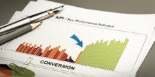 A bar graph on a document labeled 'KPI / Key Performance Indicator' shows an upward trend in conversion rates, with bars transitioning from red to green, indicating improvement. A blue arrow points to the rising green bars. A pen and paperclip rest on the document.