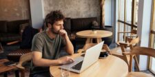 Man thoughtfully working on a laptop in a cozy cafe setting, symbolizing focus and reflection on important financial lessons for freelancers and entrepreneurs.