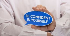 Person holding a blue speech bubble that reads 'Be Confident in Yourself,' symbolizing the theme of self-help books on confidence and self-assurance.