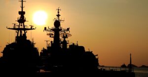 Silhouette of Navy ships at sunset with a calm ocean backdrop, symbolizing the strength and resilience of Navy SEALs, as captured in motivational Navy SEAL quotes.