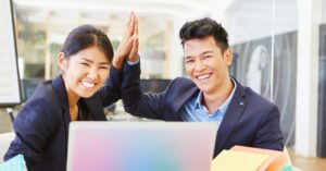 Two smiling business professionals in a modern office, high-fiving in front of a laptop, symbolizing a successful partnership, possibly representing the dynamic collaboration between a technical co-founder and another team member.