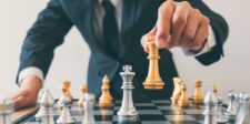 Close-up of a man in a suit moving a gold king chess piece on a chessboard, symbolizing strategic decision-making.