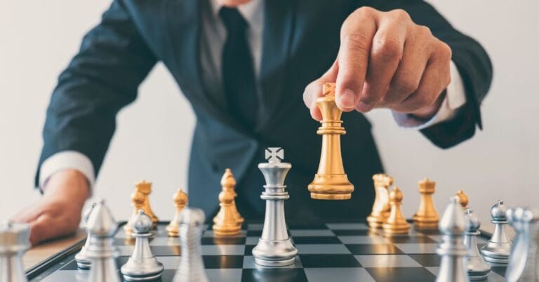 Close-up of a man in a suit moving a gold king chess piece on a chessboard, symbolizing strategic decision-making.